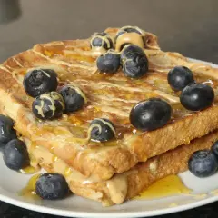 Goldbrauner French Toast Protein-Stapel mit Erdnussbutter, Honig und Blaubeeren.