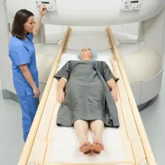 Pacjent leży na stole do rezonansu magnetycznego, pielęgniarka przygotowuje badanie. Rezonans biodra pomoże zdiagnozować problem.
