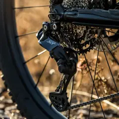 Close-up of a bicycle's rear derailleur, showcasing the Shimano Deore XT component, hinting at advanced Shimano wireless shifting technology.