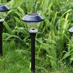 Trzy lampy solarne w ogrodzie, pokazujące, jak działa lampa solarna: panel zbiera energię słoneczną, która zasila żarówkę po zmroku.