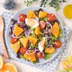 Ensalada de naranja vibrante con tomates cherry, huevo duro, cebolla morada y piñones. Una delicia fresca y colorida.