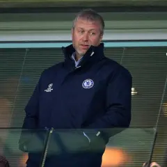 Roman Abramowicz w kurtce Chelsea FC, z emblematem Ligi Mistrzów, ogląda mecz z trybun.