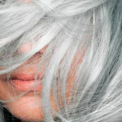 Mechas en pelo blanco natural, cubriendo parte del rostro y labios.