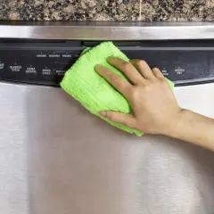 Mano limpiando un lavavajillas de acero inoxidable con un paño verde. Aprende como limpiar el acero inoxidable para mantenerlo brillante.