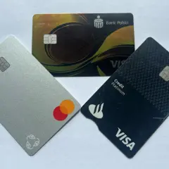 Trzy karty płatnicze: srebrna z logo Mastercard, czarna z napisem Visa Credit Platinum i złota z logo Banku Polskiego.
