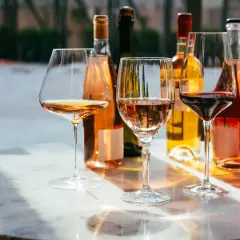 Trzy kieliszki z winem: różowym, białym i czerwonym, stoją na marmurowym stole obok butelek. Idealne na degustację wytrawnego wina.