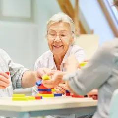 Senioren bauen mit bunten Klötzen. Ein Lächeln auf den Lippen zeigt, wie wichtig solche Aktivitäten für die demenz behandlung sind.