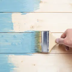Ręka w rękawiczce maluje drewniane deski na niebiesko. Czy farba do metalu można malować drewno? Eksperyment trwa.