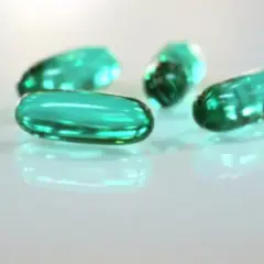 Zielone kapsułki leżą na białym tle. Czy ibuprofen jest szkodliwy? To pytanie nurtuje wiele osób.
