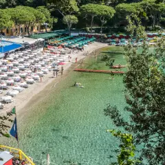 Plage animée d'une ville de la Riviera italienne, avec des parasols blancs, des chaises longues et des baigneurs dans l'eau cristalline.