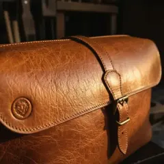 Sacoche en cuir brun, patiné par le temps, avec un fermoir et un logo lion gravé. Le cuir, c'est la qualité qui traverse les âges.