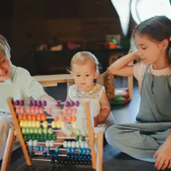 Różne grupy wiekowe w przedszkolu uczą się liczyć na liczydle. Chłopiec i dziewczynka pomagają maluchowi odkrywać świat liczb.