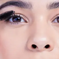 Eine Hand trägt Mascara auf die Wimpern auf, um runde Augen zu schminken.