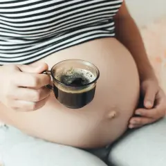 Kobieta w ciąży trzyma filiżankę kawy. Delikatny napój dla przyszłych mam.