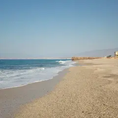 La Fabriquilla, Almería. Una playa de guijarros con el mar azul y una torre blanca solitaria.