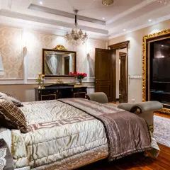 Elegancka sypialnia glamour beżowa z bogato zdobionym łóżkiem, kryształowym żyrandolem i złotymi detalami.