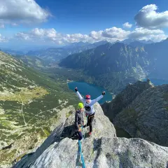 Dwóch wspinaczy na szczycie, radość po udanej wspinaczce. W tle malownicze Tatry i jezioro.