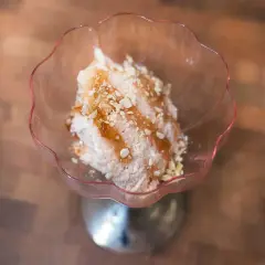 En skål med rosa rabarbersorbet toppad med nötter och sirap. En härlig sommardessert.