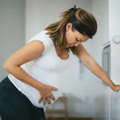 Schwangere Frau mit Hand auf dem Bauch, die sich vorbeugt. Sie fragt sich, ab wann Vorwehen auftreten können.