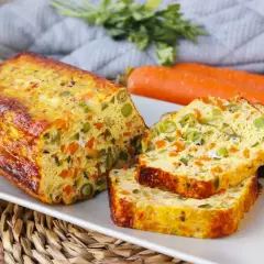 Pastel de verduras al horno, con trozos de zanahoria y guisantes, servido en una bandeja blanca.