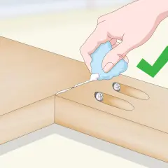 Application de colle pour assembler 2 planches en longueur. Une main tient un tube de colle, deux vis sont déjà en place.