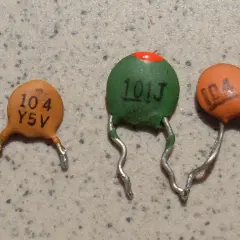 Trzy ceramiczne kondensatory z widocznymi oznaczeniami, np. "104".