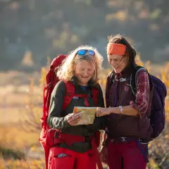 Två kvinnor med ryggsäckar planerar sin vandring i Vemdalen. Hösten färgar landskapet gyllene.