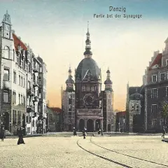 Widok na plac z imponującą synagogą w Gdańsku. Wokół kamienice, tory tramwajowe i kilka postaci spacerujących po bruku.