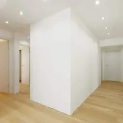 Un corridoio moderno con pavimenti in legno chiaro e una parete in cartongesso curvo che crea un effetto dinamico.