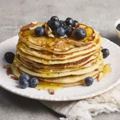 Stapel goldbrauner Pancakes, garniert mit Blaubeeren, Mandelsplittern und Honig. Ein köstliches Rezept für High Protein Pancakes.