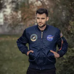 Mężczyzna w granatowej kurtce bomberce Alpha Industries z naszywkami NASA i misji wahadłowca. Alpha Industries to firma znana z odzieży inspirowanej lotnictwem.