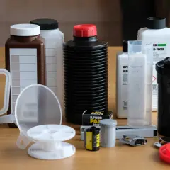 Zestaw do wywoływania klisz: butelki z chemikaliami, w tym **fixer**, menzurki, klisza, bębenek i akcesoria.