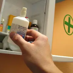 Ręka wyjmuje z apteczki butelkę z napisem "Hydrogenium peroxydatum 3% (Wodoru nadtlenek 3%) Syn. Woda utleniona". Idealna do walki z pleśnią.