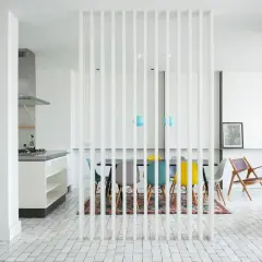 Un divisorio a listelli bianchi separa la cucina moderna da una zona pranzo con sedie colorate. Un'idea per come riempire spazio tra cucina e muro.
