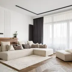 Nowoczesny salon z beżową sofą i puszystym dywanem. Elegancki karnisz do zabudowy dyskretnie podkreśla zasłony.