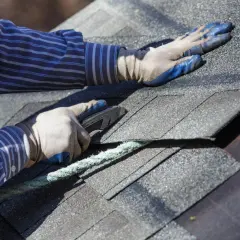 A roofer uses a utility knife to cut shingles, a step in how to dispose of shingles properly after removal.