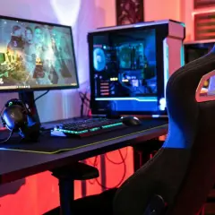 Gaming-Setup mit beleuchtetem PC, Tastatur und Kopfhörern. Der **Atlas OS**-Desktop zeigt ein Spiel.