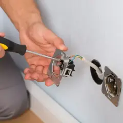 Instalator przykręca gniazdko, pokazując, jak zmostkować gniazdko. Widać przewody i śrubokręt.