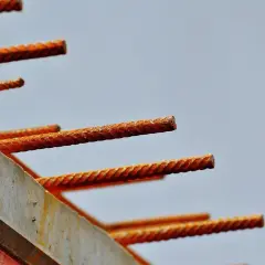 Zardzewiałe pręty zbrojeniowe wystające z betonowej formy na tle jasnego nieba.