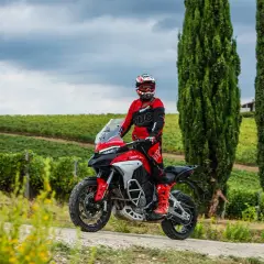 Un motociclista in tuta rossa sfreccia tra i vigneti toscani, godendosi le strade più belle della Toscana in moto.