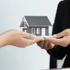 Manos intercambian una maqueta de casa, simbolizando la gestión de alquileres y la transferencia de propiedades.