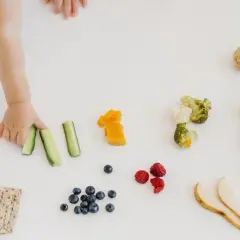 Mano di bimbo afferra bastoncini di cetriolo, parte di un pasto con tagli sicuri svezzamento: frutta, verdura e cracker.