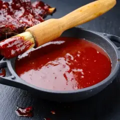 Pędzel z sosem barbecue zanurzony w miseczce, obok żeberka. Idealny sposób, jak zrobić sos barbecue.