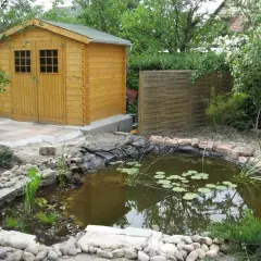 Un bassin d'agrément avec des nénuphars, une cabane en bois et une clôture en bois créent un espace paisible, préservant l'intimité du voisin.