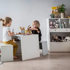 Uroczy kącik dla dziecka w salonie. Dwie dziewczynki rysują przy białym stoliku, otoczone pluszakami i książkami.