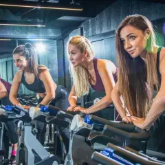 Cztery kobiety intensywnie wykonują ćwiczenia cardio na rowerach stacjonarnych w siłowni.