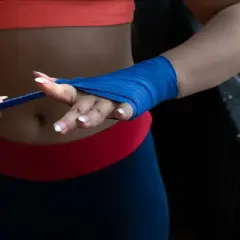 Une femme en tenue de sport prépare ses mains pour l'entraînement, montrant comment mettre des bandes de boxe bleues.