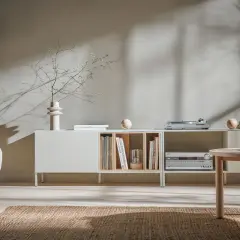 Miękkie światło pada na ściany w kolorze kaszmirowym, oświetlając salon z minimalistyczną komodą i wygodną sofą.