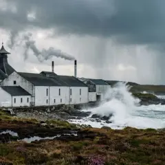 Distillerie sur l'île d'Islay, battue par les vagues et la pluie sous un ciel orageux. La fumée s'échappe d'une cheminée.