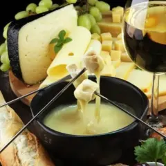 Un délicieux vin accompagne une fondue au fromage, avec du pain, des pommes de terre et de la charcuterie.
